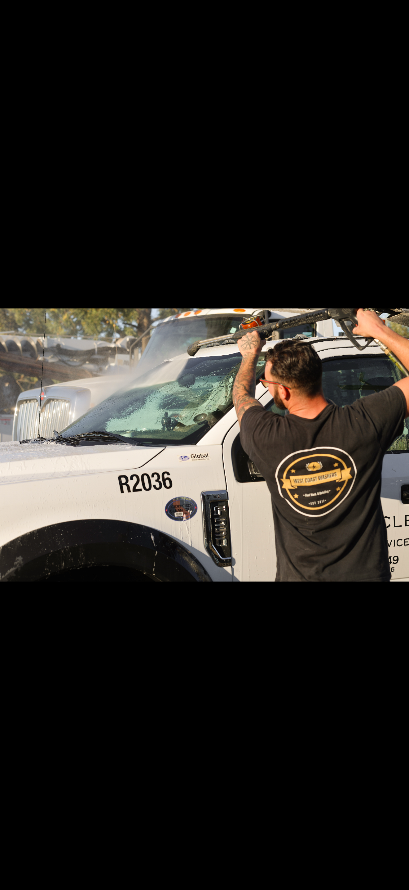 Worker pressure washing a commercial truck windshield